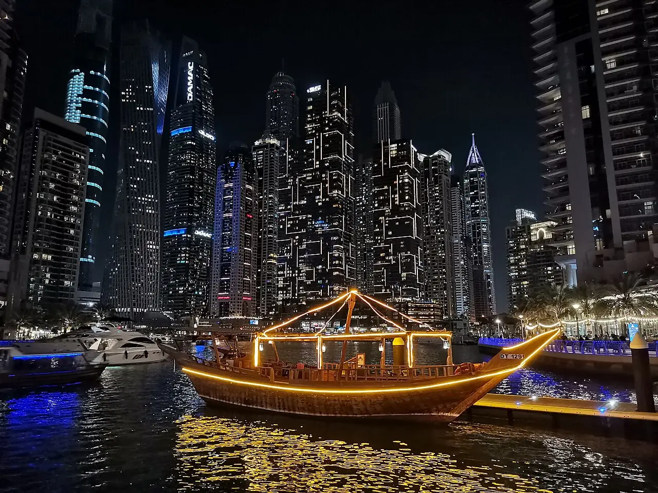 An illuminated dhow cruising past the Dubai Marina towers at night