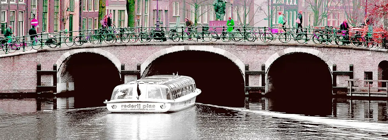 A canal boat passing under a bridge in Amsterdam
