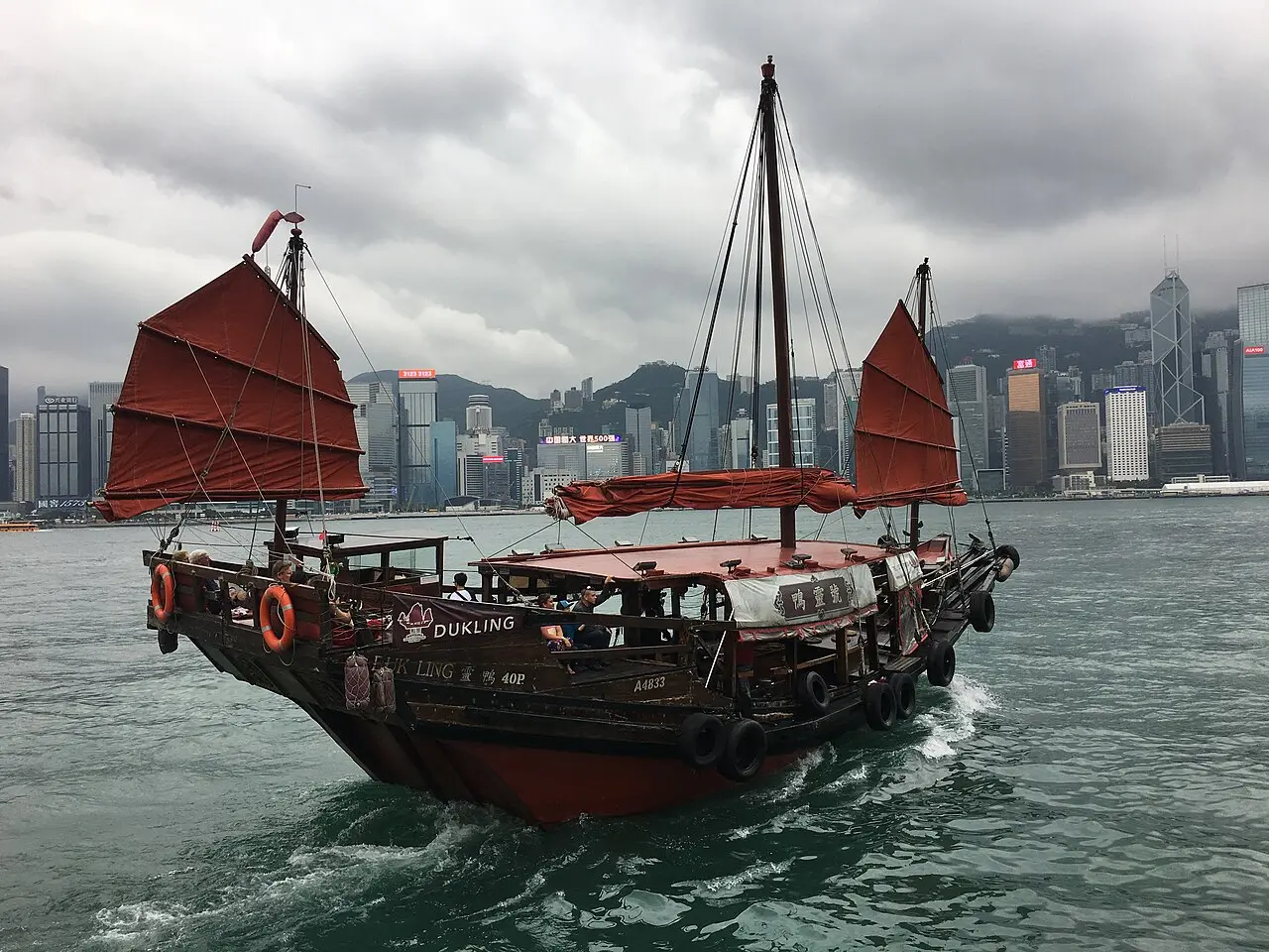 A red-sailed junk under full sail on the harbour