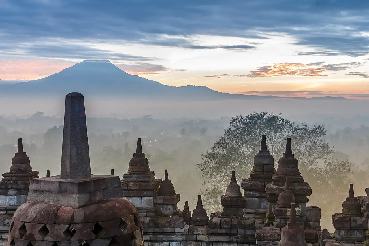 The stupas of Borobudur at dawn with mist and volcanoes