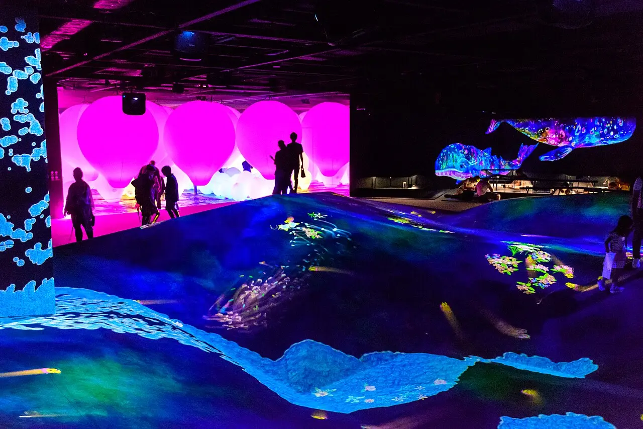 Digital whales and flowers projected across a room at teamLab Borderless
