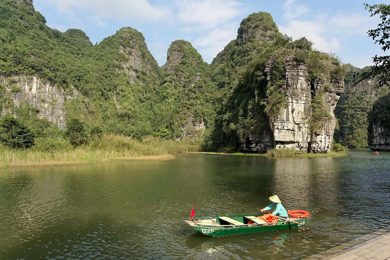 A boatwoman rowing beneath limestone cliffs at Trang An